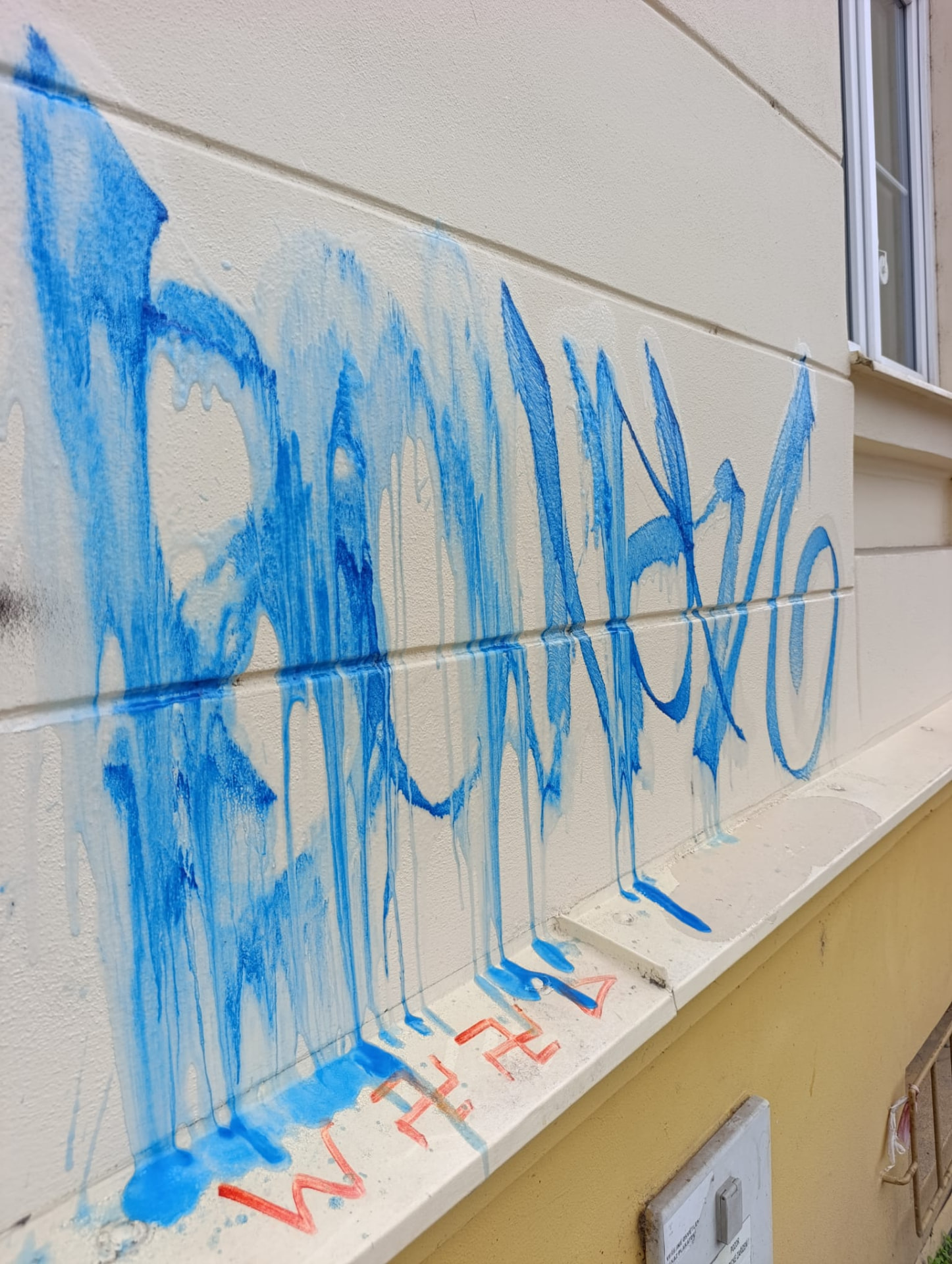 Modré graffiti so stekajúcou farbou na fasáde bytového domu