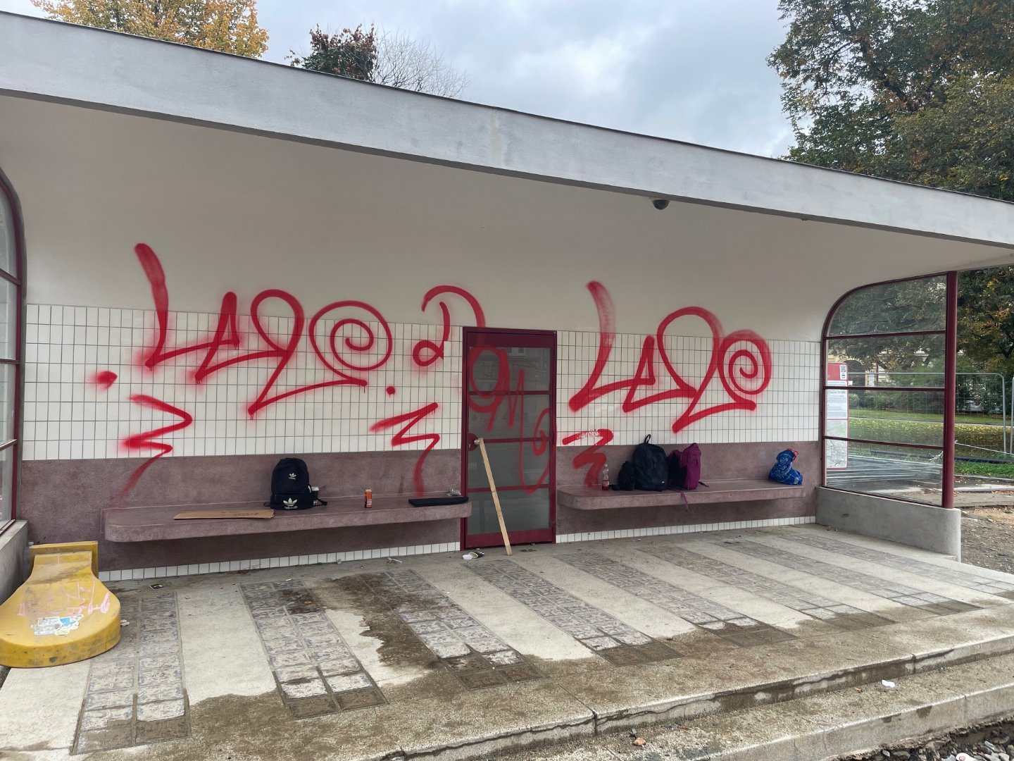 Červené graffiti na obklade a stene prístrešku pred zásahom