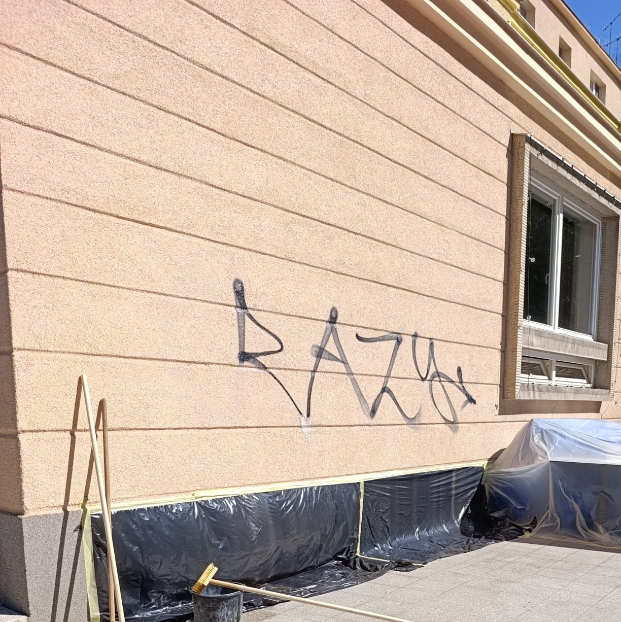Čierne graffiti na štruktúrovanej fasáde pred odstránením